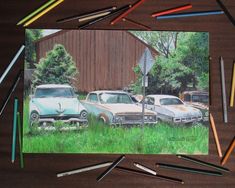 some colored pencils are laying on the ground next to an image of old cars