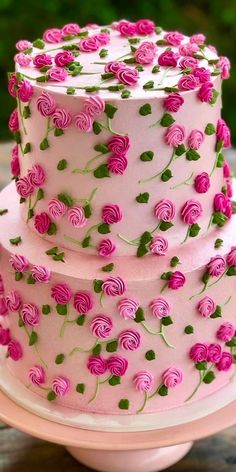 a three tiered cake with pink roses on the top and green leaves on the bottom