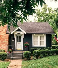 a small black and white house with an american flag in the front yard