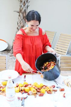 a woman in an orange dress is cooking corn on the cob and sausages