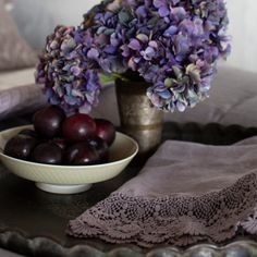 purple flowers and plums in a bowl on a table