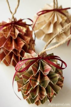 two paper pine cones with red ribbons tied to them on a white surface, one hanging from a twine of twine