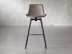 an upholstered bar stool with a black metal frame and seat, in front of a concrete wall