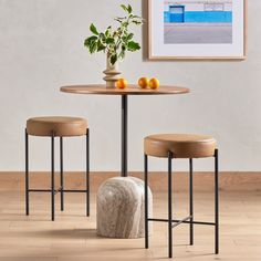 two stools and a table with fruit on it in front of a white wall