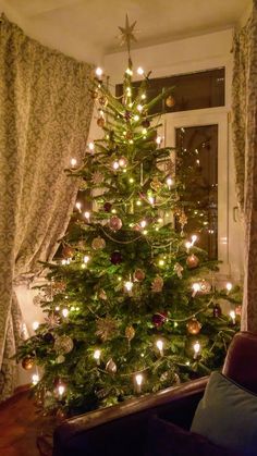 a small christmas tree is lit up in front of a window with curtains and drapes