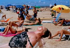 many people are laying on the beach with umbrellas and sunbathers in the background