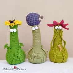 three crocheted vases with faces and flowers on them, one is wearing a hat