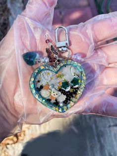 a hand holding a heart shaped keychain filled with lots of different things in it