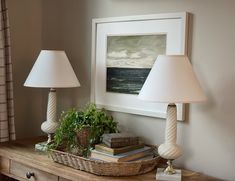 two lamps sitting on top of a wooden table next to a basket filled with books