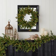 a christmas wreath on top of a dresser next to candles and other holiday decorations in front of a mirror