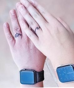 two hands holding each other with tattoos on their fingers and wristbands, one has a small bird tattoo on it's left hand