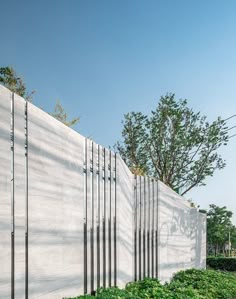 a white wall with metal bars on the side and green plants growing in front of it