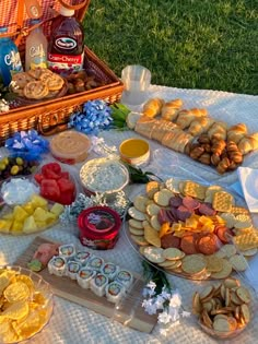 an assortment of food is laid out on a picnic blanket in front of the grass