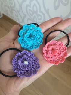 three crocheted flower hair ties are shown in the palm of someone's hand