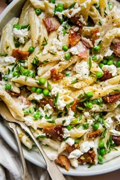 a pasta salad with peas, bacon and cheese on a white plate next to silverware