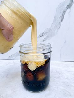 a person pouring ice cream into a mason jar with text overlay that reads at - home pumpkin cream cold foam