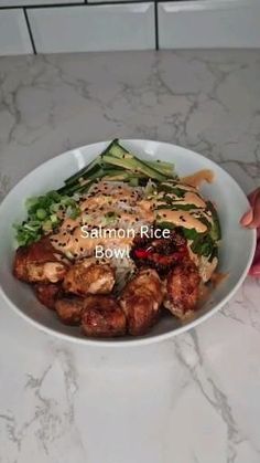 a bowl filled with meat and vegetables on top of a marble countertop next to a woman's hand