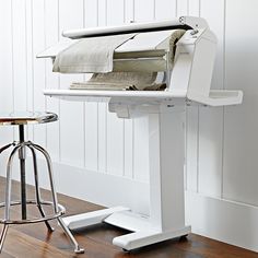 a white desk with an ironing board attached to the wall and a stool next to it