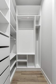 an empty walk in closet with white shelving and wood flooring on the side