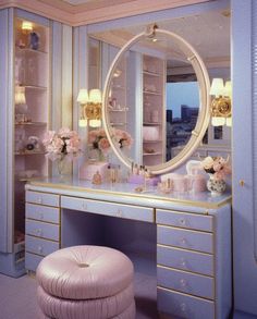 a dressing table with a mirror and stool in front of it, surrounded by pink flowers