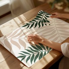 a person sitting at a table with a piece of paper on it that has leaves painted on it