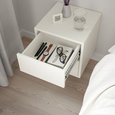 a white bedside table with glasses, pens and pencils