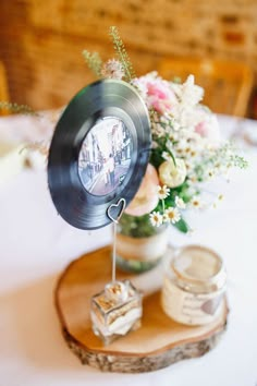 an old record on a wooden stand with flowers in the vase and other items around it