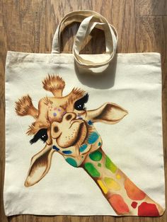 a colorful giraffe painted on a white tote bag sitting on top of a wooden floor