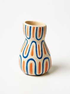 an orange and blue vase sitting on top of a white table