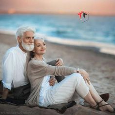 an older couple is sitting on the beach