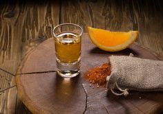 a glass of tea next to an orange slice on a wooden board with a burlock