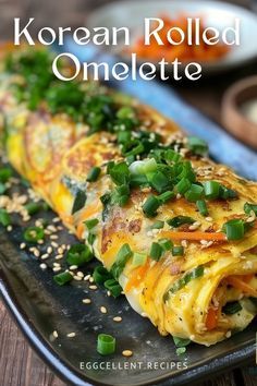 korean rolled omelette on a black plate with green onions and sesame seed sprinkles