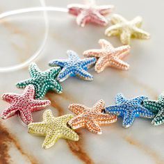 five starfish charms are sitting on a marble surface, one is multicolored and the other has white string