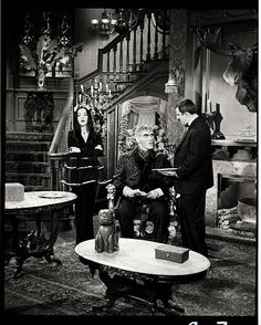 an old photo of three people in a living room talking to each other while another woman looks on