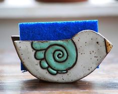 a blue and white brooch with a snail on it's side sitting on a wooden table