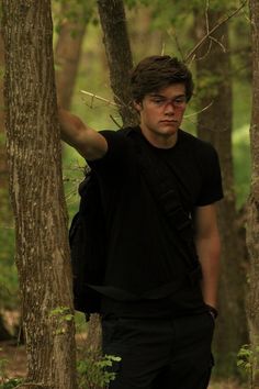 a man standing next to a tree in the woods