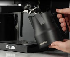 a person is holding a coffee cup in front of an automatic coffee maker with the word dualt on it