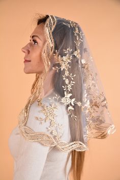 a woman wearing a wedding veil with flowers on the side and gold trimmings