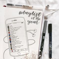 an open notebook with the words playlist of the year written on it next to some pens