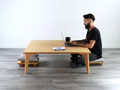 a man sitting at a wooden table with a laptop on his lap and looking at the screen