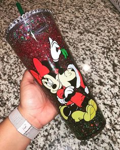 a hand holding a mickey mouse tumbler on top of a granite counter with a green straw in it