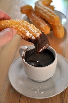 a person dipping some kind of chocolate in a cup with churros on the side