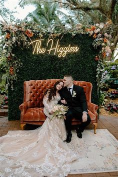 a bride and groom are sitting on an orange couch in front of a neon sign