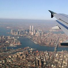 the wing of an airplane flying over a large city and river with tall buildings on both sides