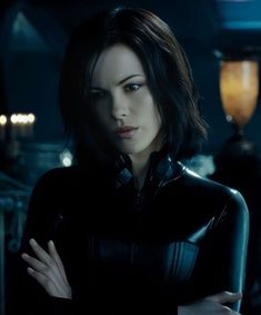 a woman with dark hair and black catsuits standing in a dimly lit room