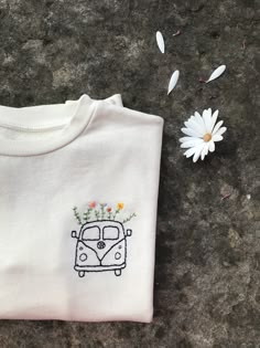 a white t - shirt with flowers and a car embroidered on the front sits next to a daisy