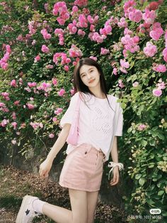 a young woman standing in front of pink flowers with her hand on her hip and looking at the camera