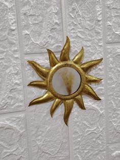 a gold sun shaped mirror hanging on the side of a white wall with decorative tiles