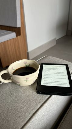 a cup of coffee sitting next to an electronic device on top of a table in a room