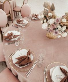 the table is set with plates and napkins, silverware, and pink flowers